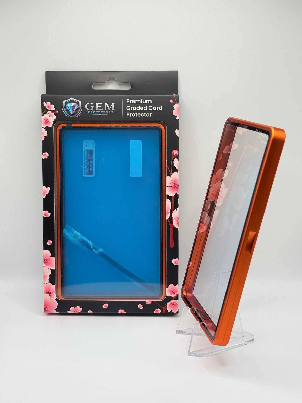 Orange Gem Protectors case angled on a clear stand to show the frame's side profile, next to its retail box