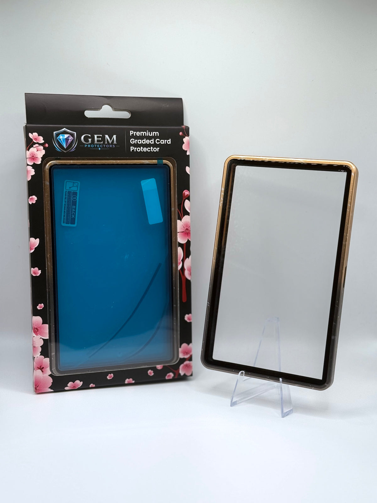 Front view of the empty Black & Gold Speckle Gem Protectors case showing the frame and clear panel, beside its retail box