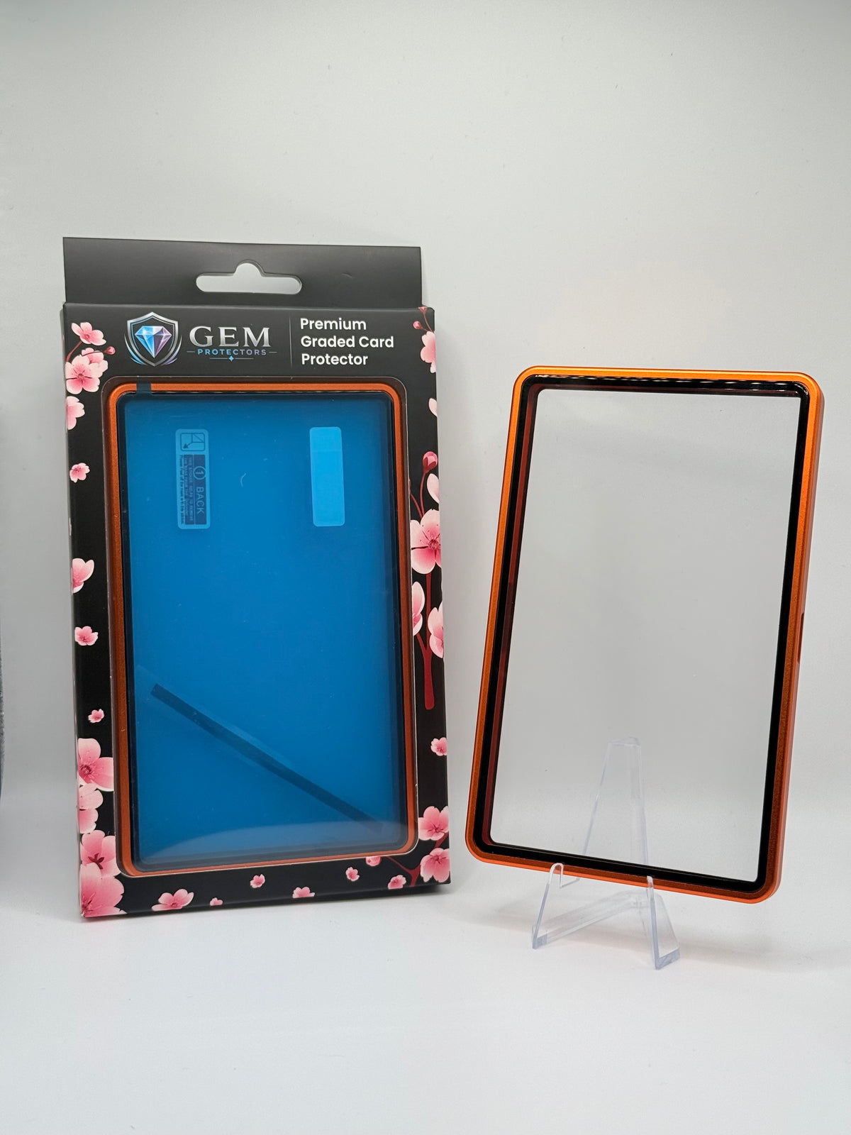 Orange Gem Protectors magnetic PSA slab case standing upright on a clear stand next to its retail box