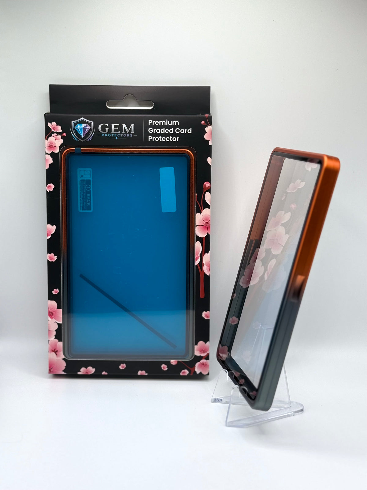 Black & Orange Gem Protectors case angled on a clear stand to show the frame's side profile, next to its retail box