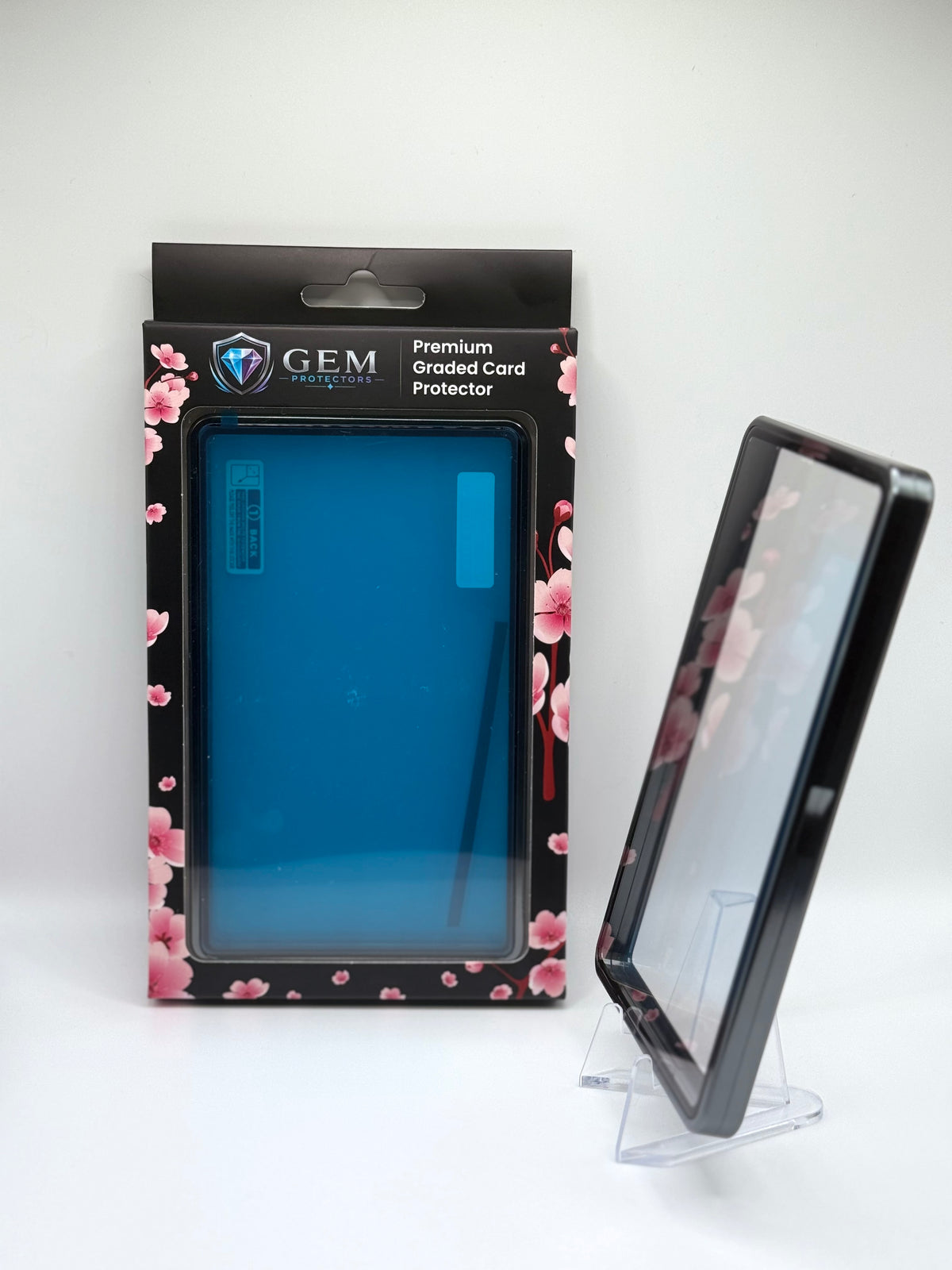 Charcoal Gray Gem Protectors case angled on a clear stand to show the frame's side profile, next to its retail box