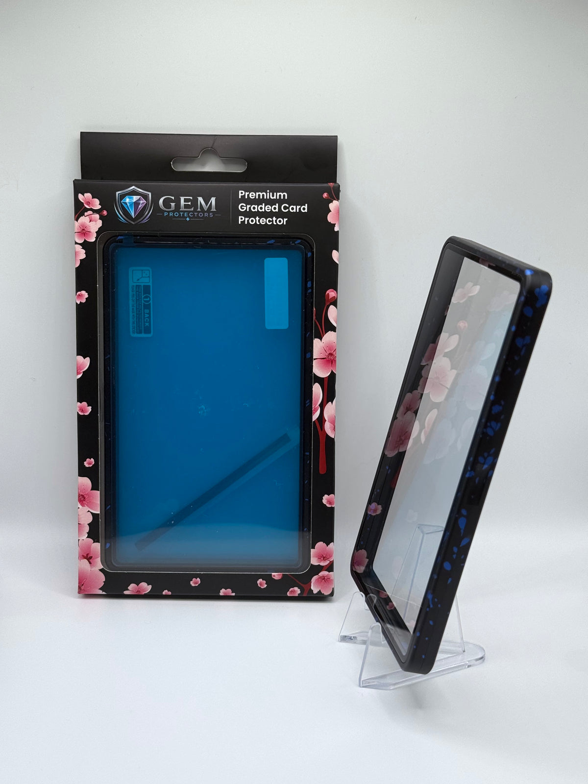 Blue Speckle Gem Protectors case angled on a clear stand to show the frame's side profile, next to its retail box
